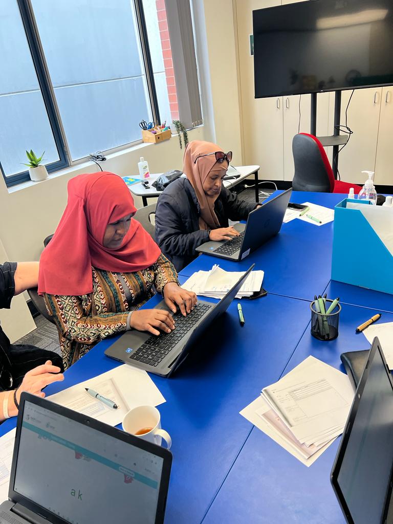 Two women wearing hijabs type on laptop computers